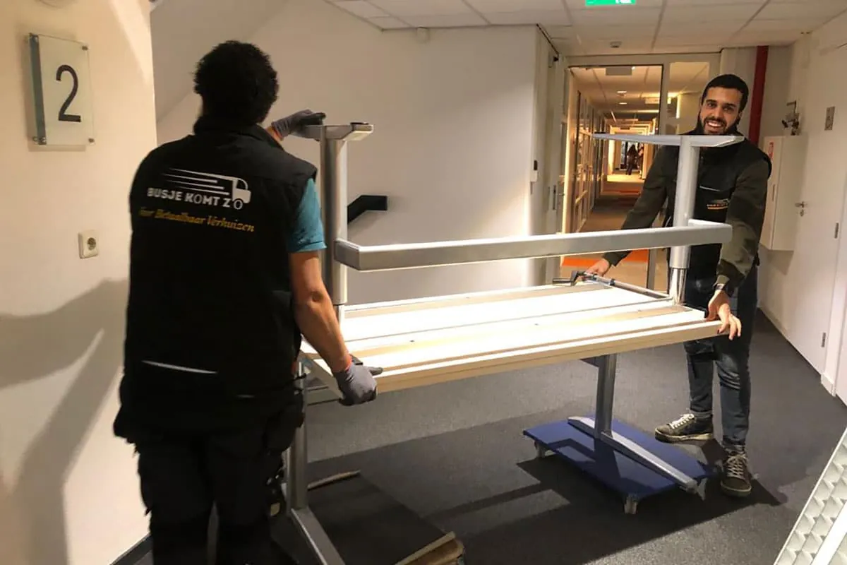 Twee verhuizers van Busje komt zo dragen een bureau door een kantoorgang